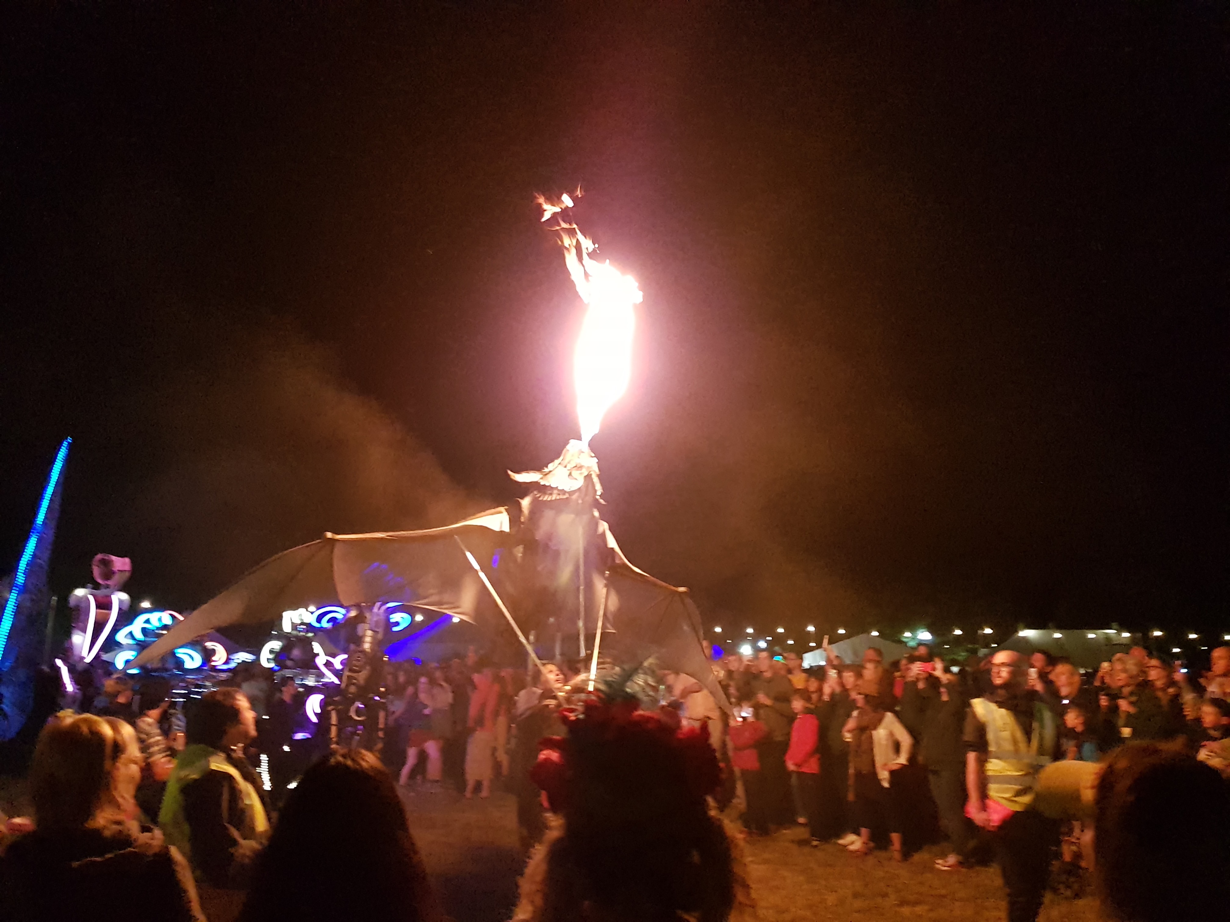 A large firebreathing bat controlled by a person using levers as a crowd stands around watching