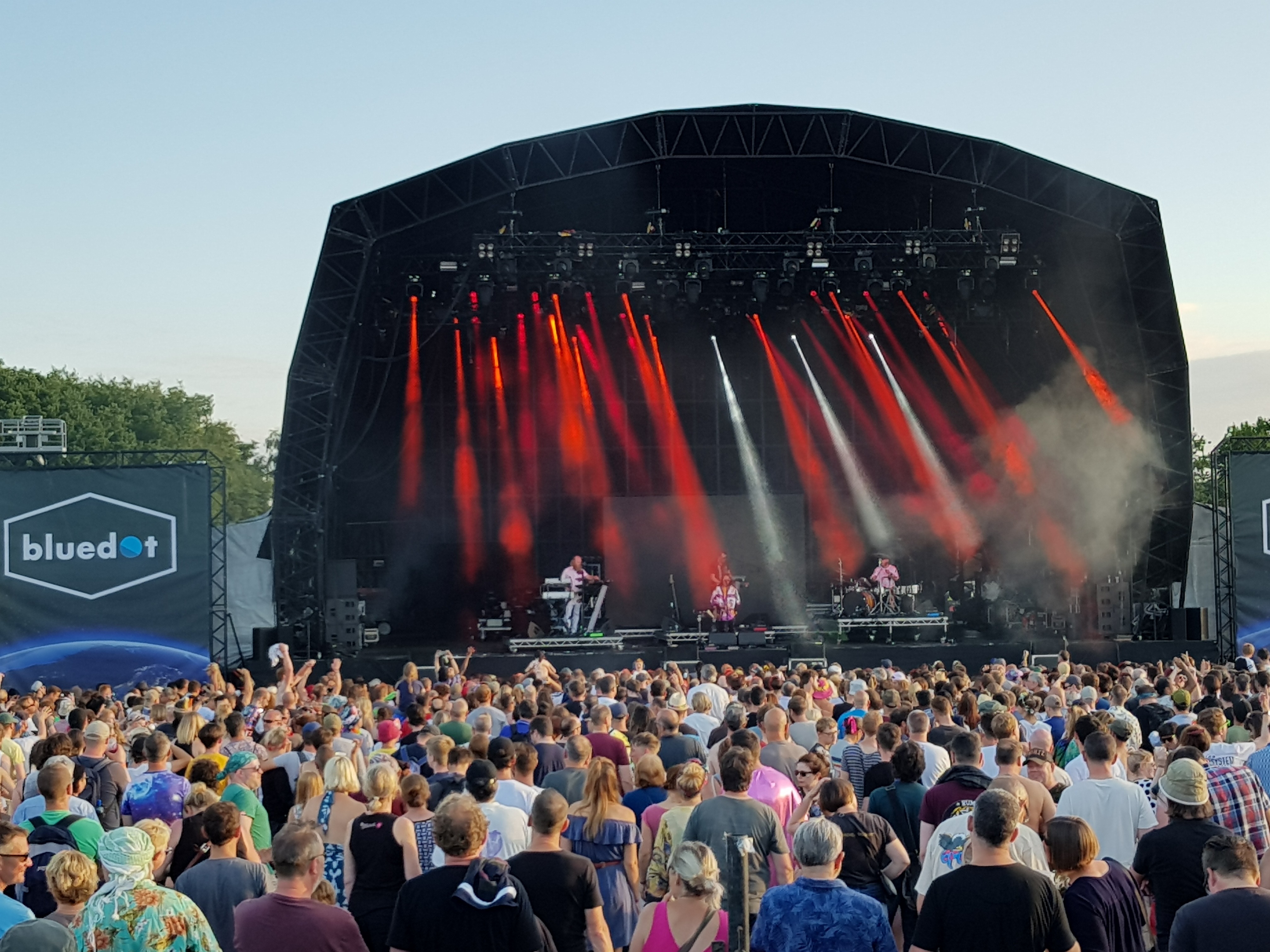 A large number of people standing in front of a big stage as a band is performing