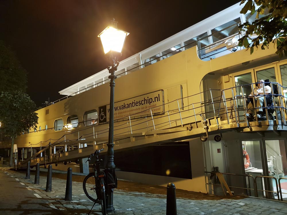 Night view of an accessible canal cruise ship with a ramp leading to the entrance, street lamp illuminating the scene.