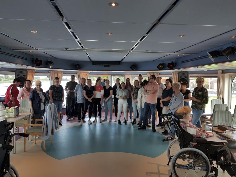 Group of people gathered on the Prins Willem Alexander ship's interior, showing a mix of guests and crew in a lively atmosphere.