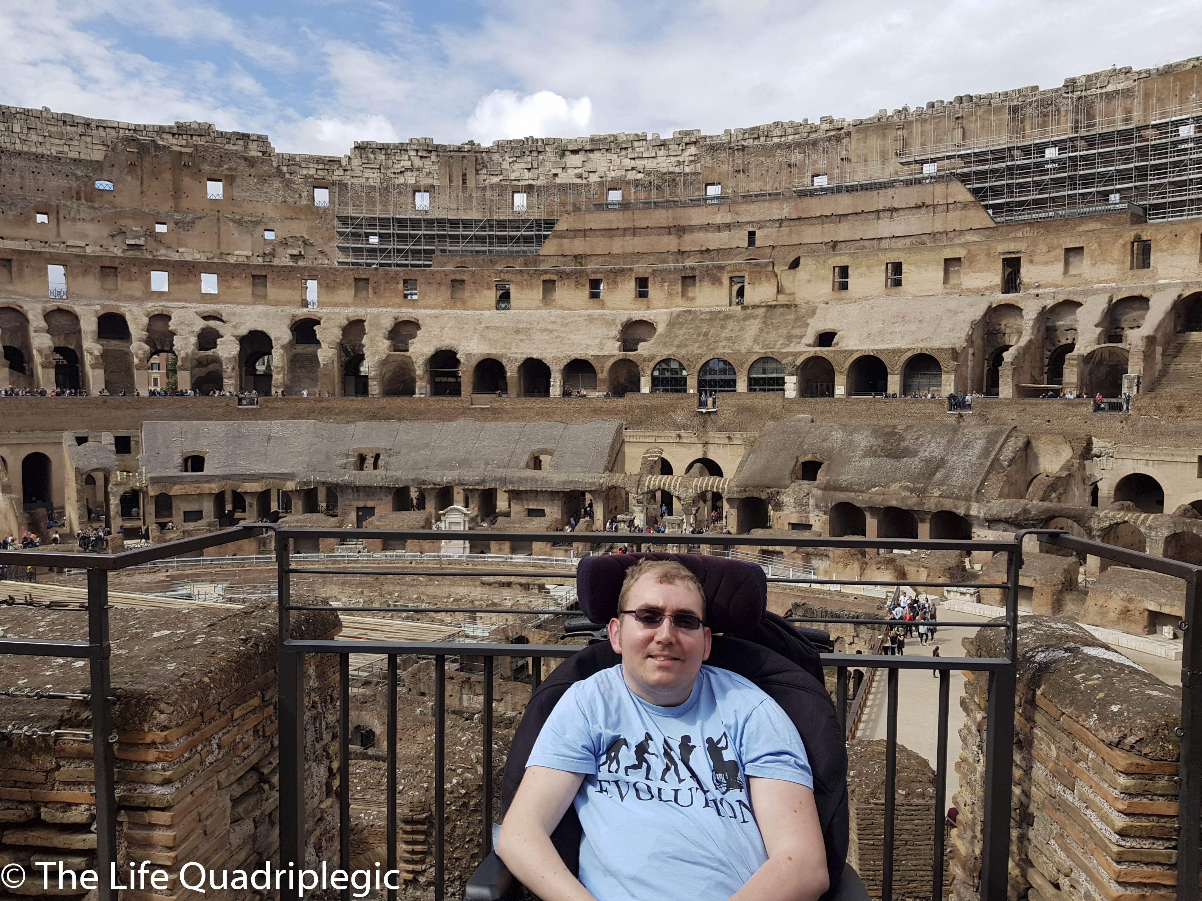 Person in a wheelchair posing in front of the Colosseum in Rome, showcasing the ancient structure's interior and surroundings.