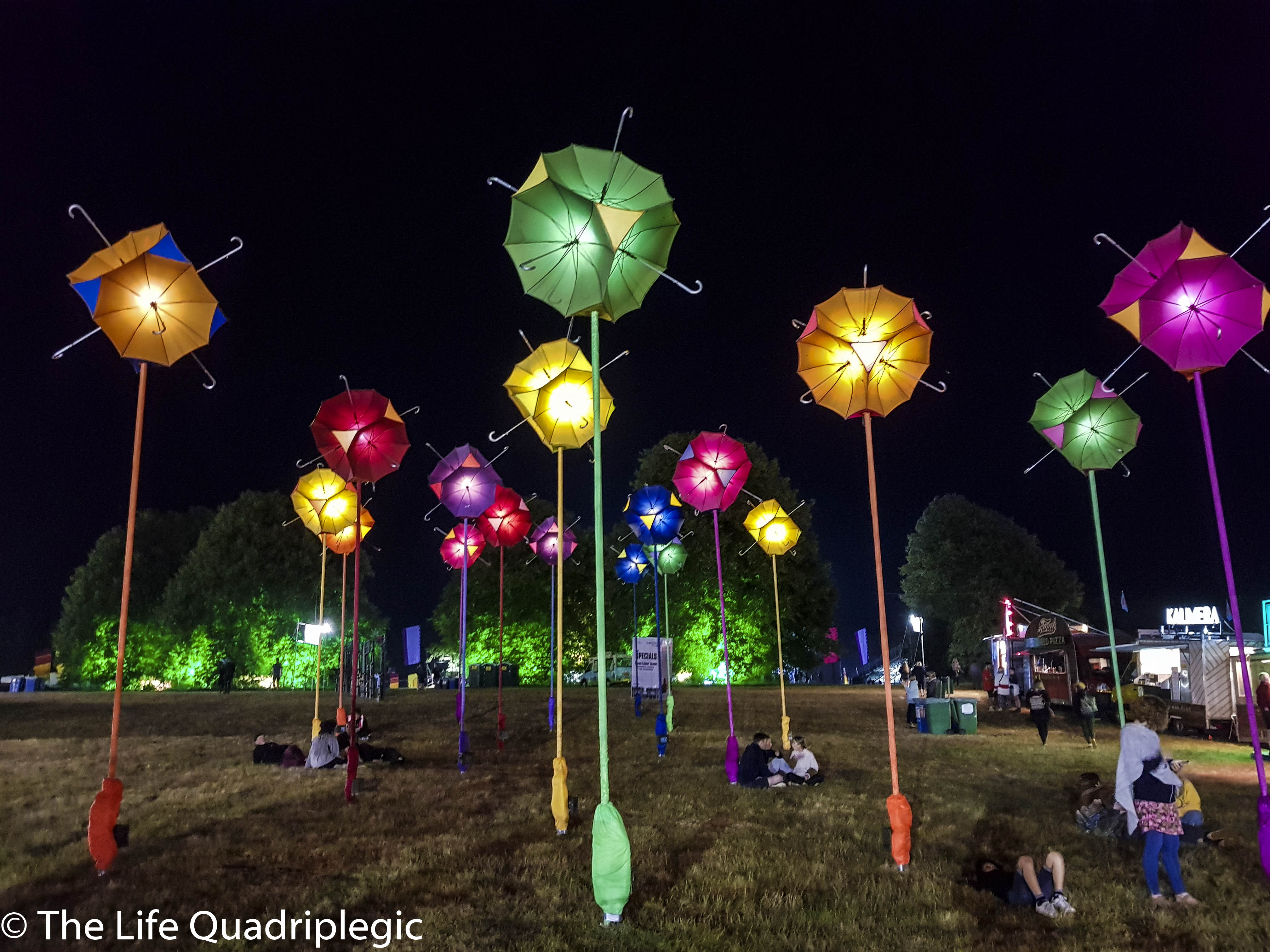 15 different posts are erected vertically in a gratis field each one a different colour. On top of each post are four umbrellas arranged so that there handles point in opposite directions to each other.