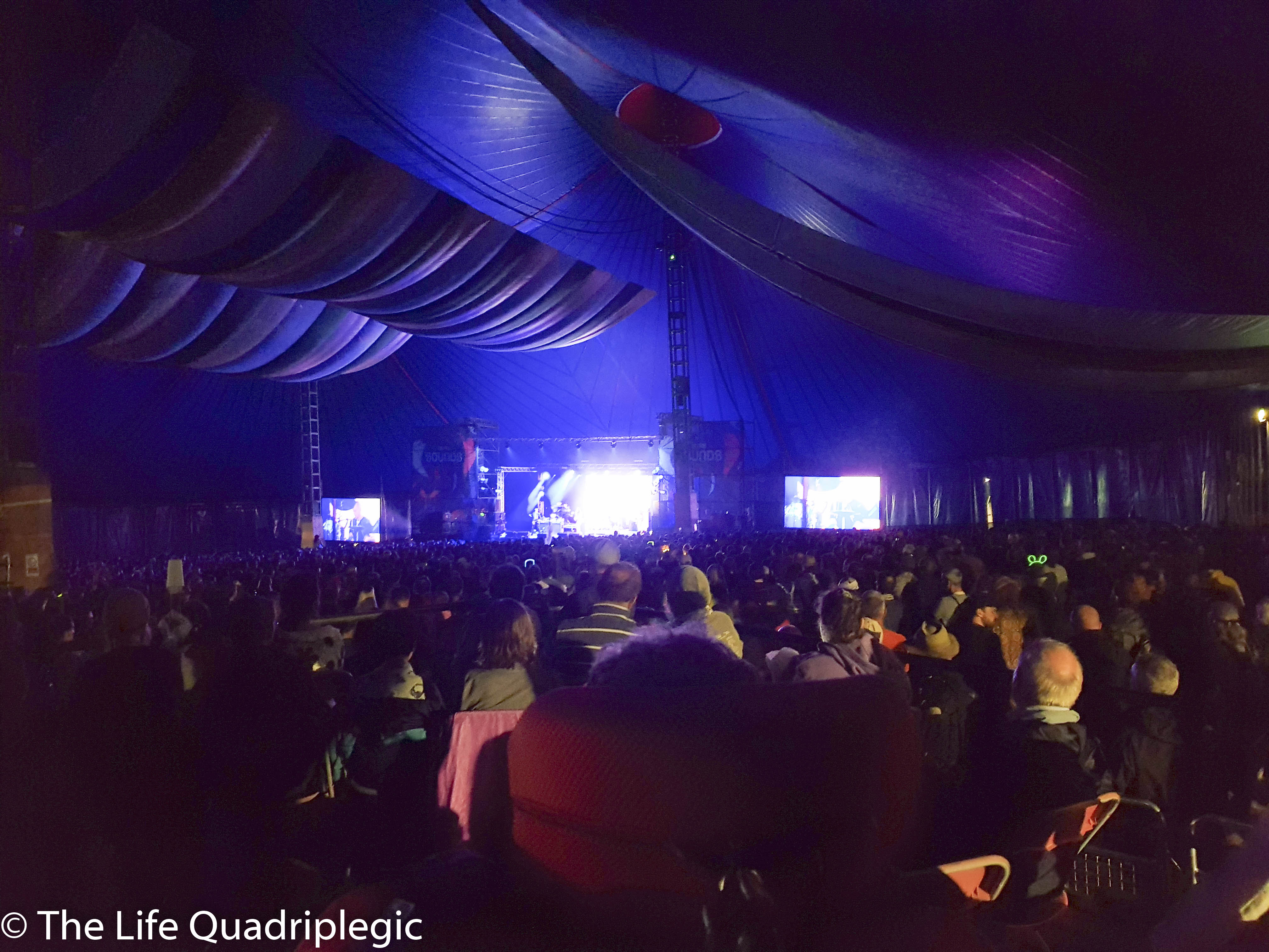 He shot over the top of large crowd, Inside a tent with a stage in the background.