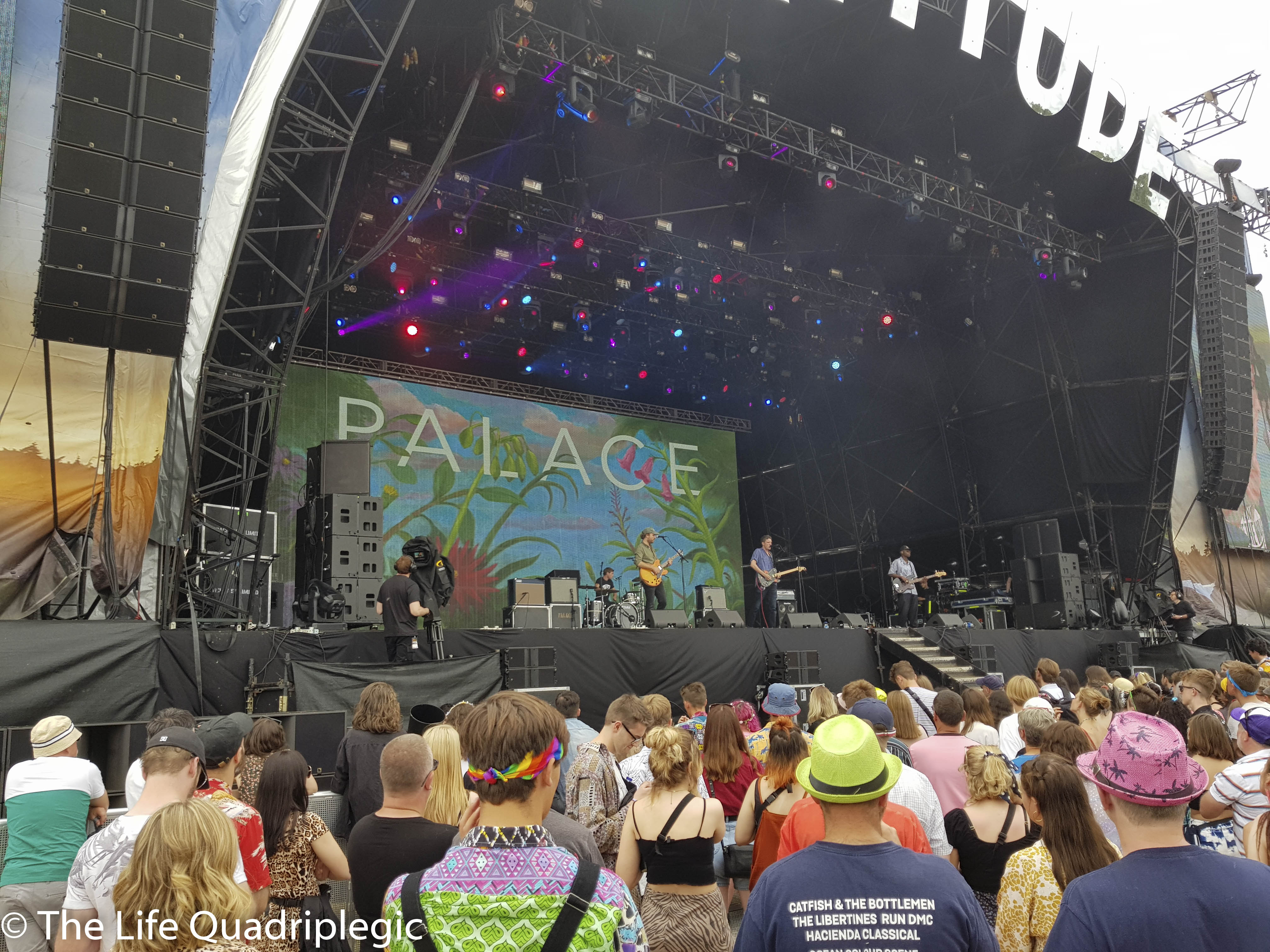 3 men are stood on a stage playing electric guitars with a large crowd