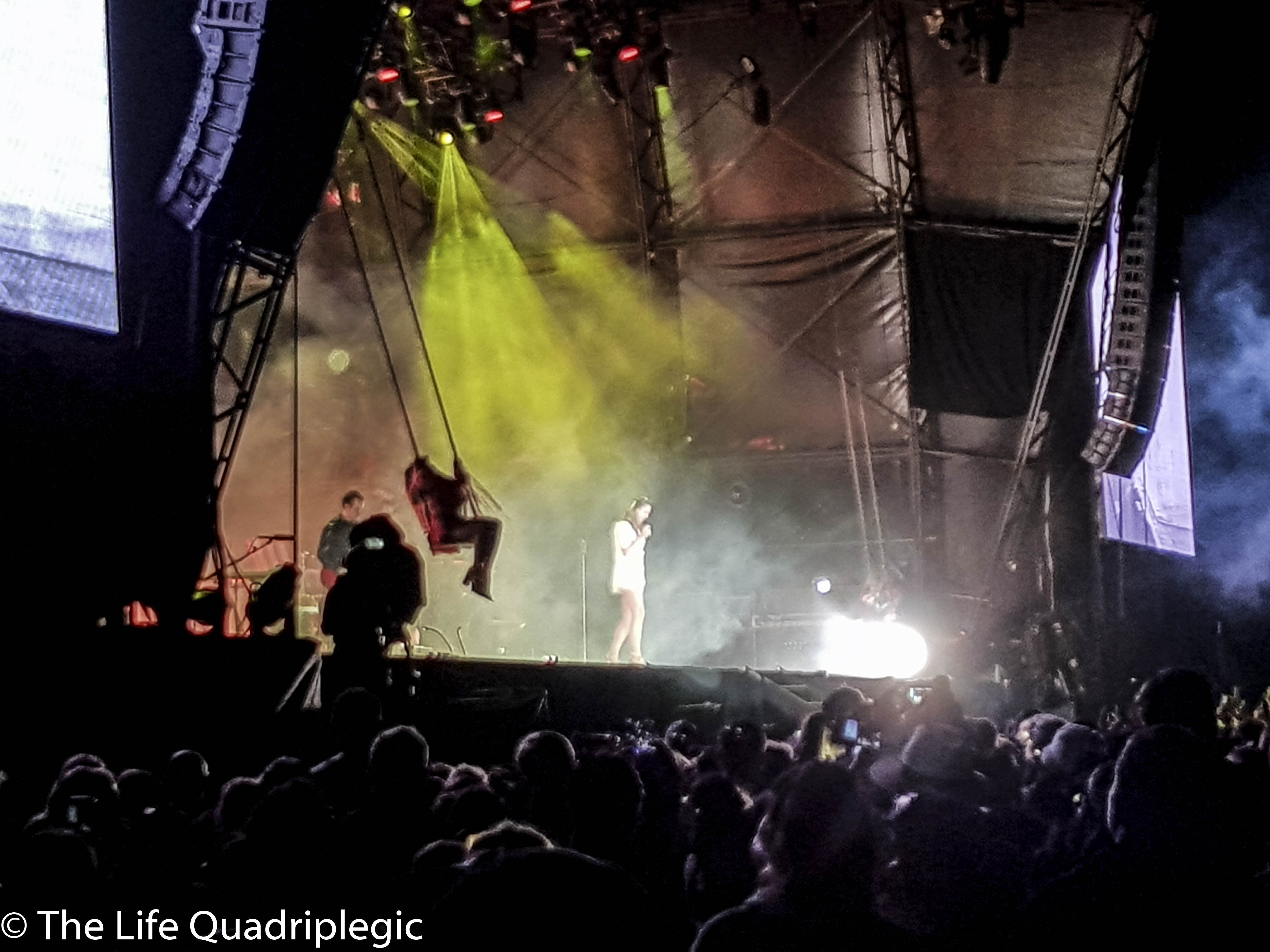 A lady stands on stage holding a microphone with a large crowd in front of it watching her