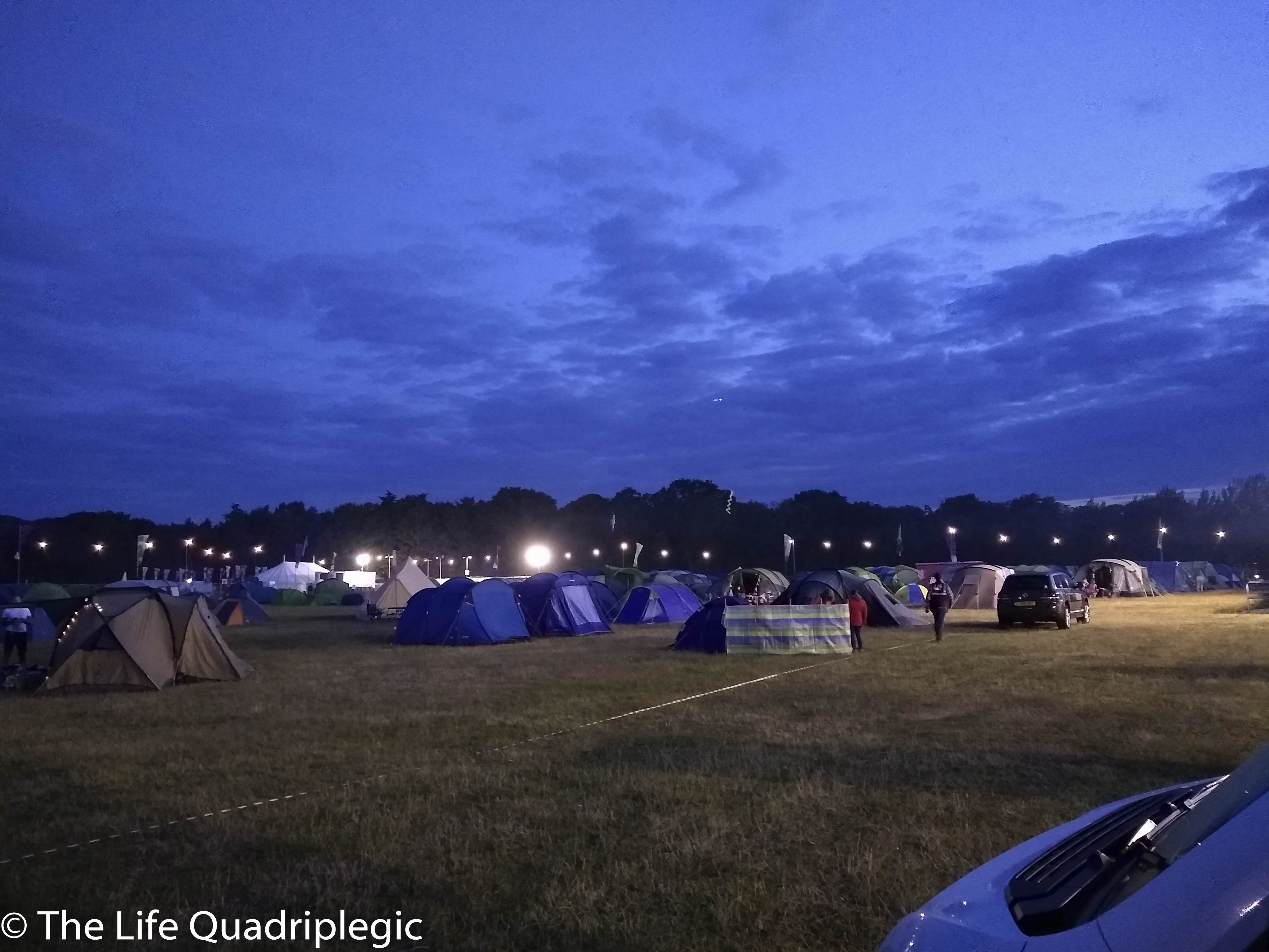 A night time shot lots of tents in a grassy field with a line of trees in the background