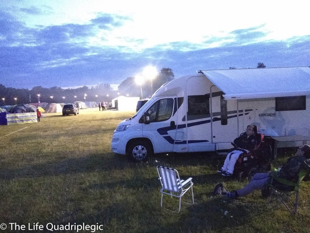 A side view of a motorhome with a young man in a powerchair sat next to it and another man in a camping chair