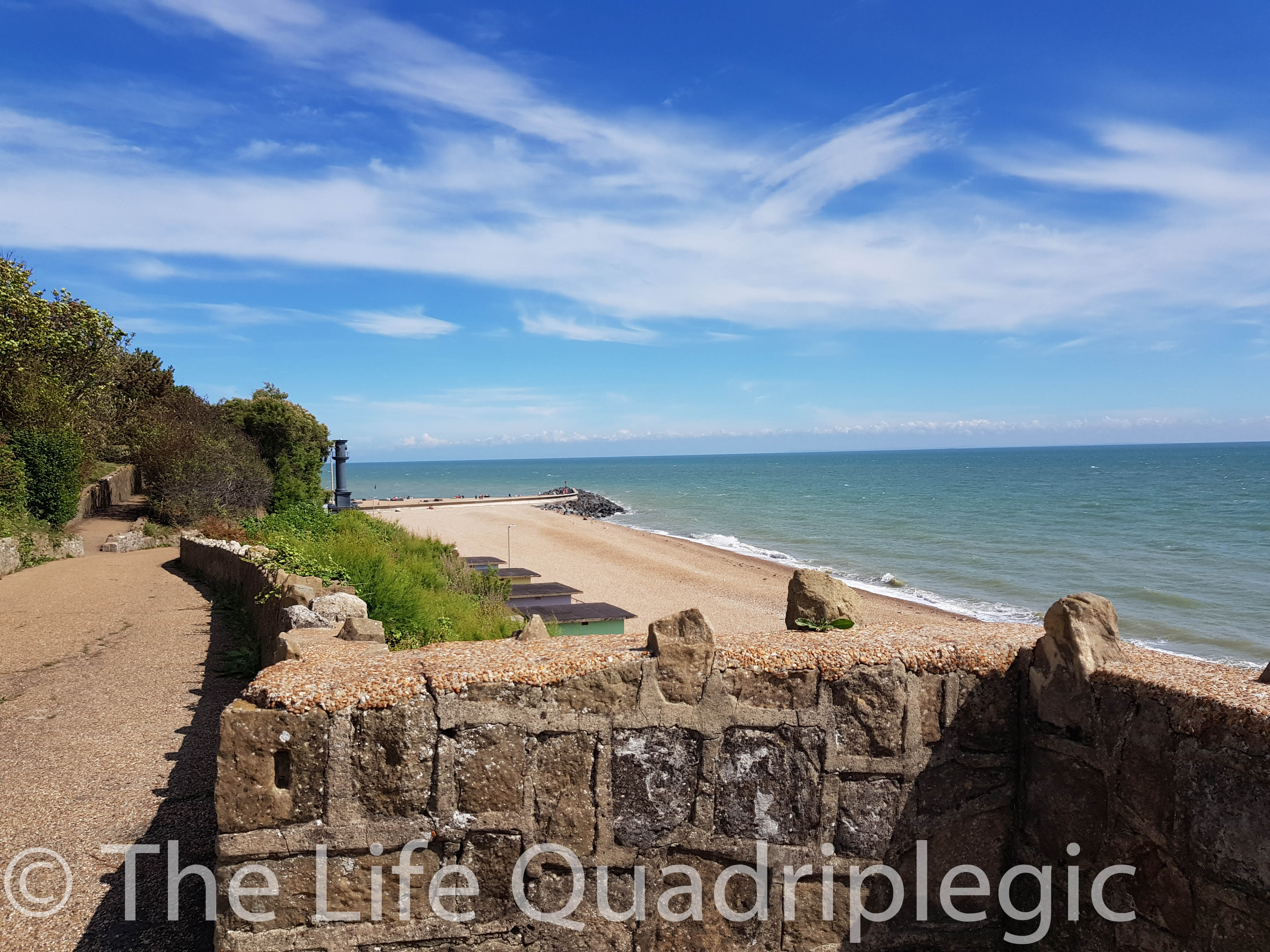 Looking over a stone wall at the beach with sea on the right side of the image