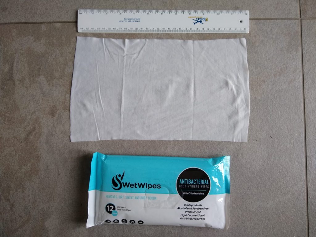A packet of SwetWipes with a wipe laid out next to it. A ruler lays next to the wipe for reference. The wipe is as long as the ruler.