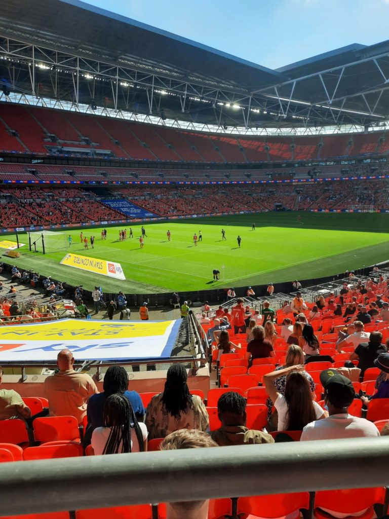View of a football pitch where players on it with people spread out in the stands surrounding it