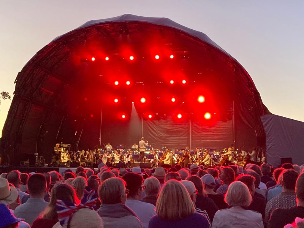 A performance by the Royal Philharmonic Orchestra with red stage lighting, viewed from the audience at the Leeds Castle concert.