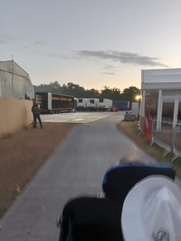 The back of a power chair user driving along a metal walkway towards an area with parked lorries next to each other.