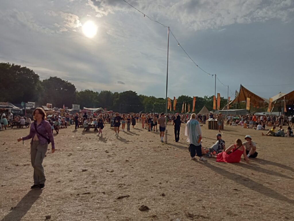 A busy festival scene with people walking around enjoyng the atmosphere, food stalls in the background, and a partly cloudy sky.