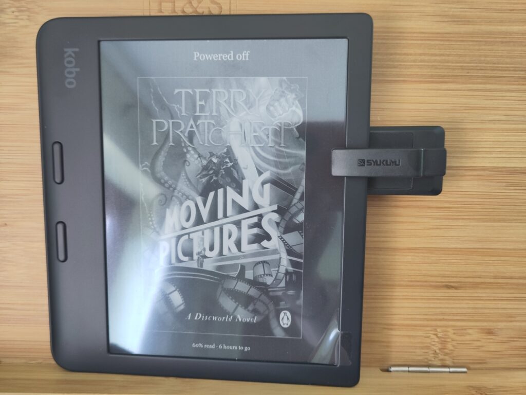 An e-reader on a wooden book stand with a small black rectangular clip on the side of the e-reader