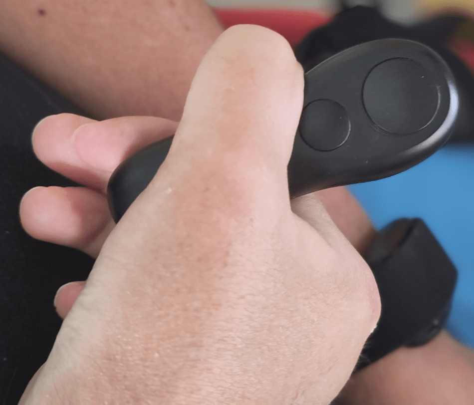 A hand holding the remote control between the thumb and fingers with both buttons above the thumb