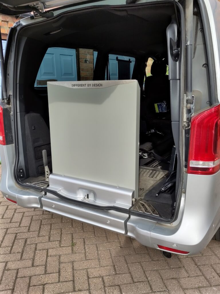 Rear view of a Mercedes V250 wheelchair accessible vehicle, featuring an open back door and an upright ramp labeled 'DIFFERENT BY DESIGN'. The vehicle interior is visible, showcasing a spacious design suitable for wheelchair access.