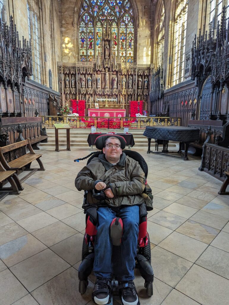 A man in a wheelchair sitting inside a large, ornate church with stained glass windows and an altar in the background.
