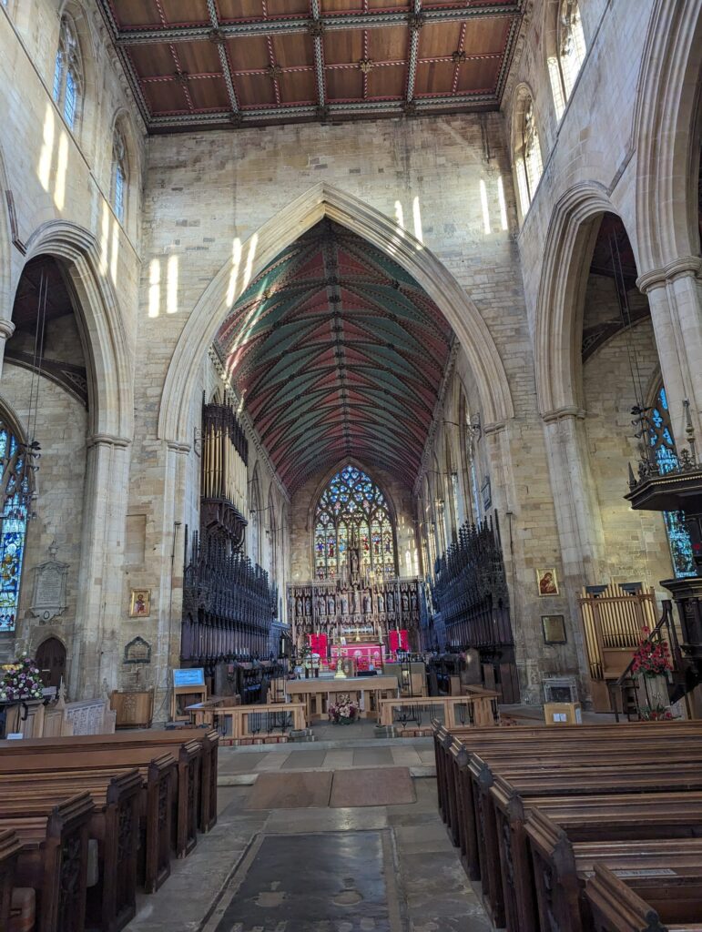 Interior view of Saint Botolph's Church, known as Boston Stump, showcasing its tall arched ceilings, intricate wooden beams, and vibrant stained glass windows.