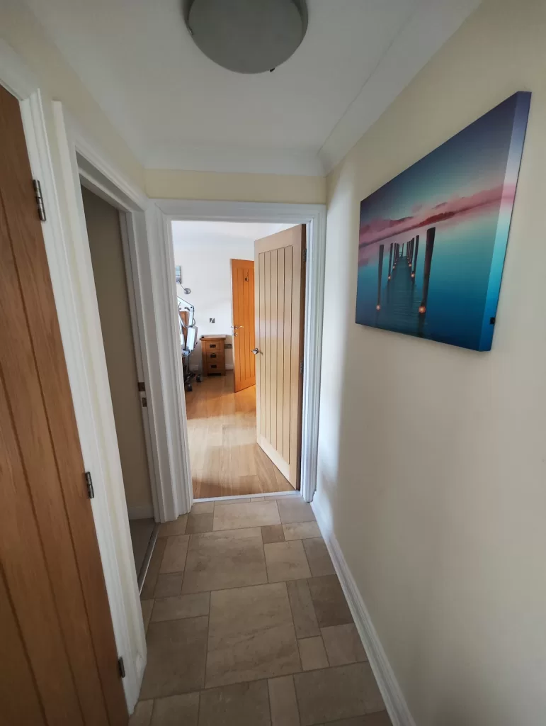 A hallway inside Clementine Cottage, showing doorways to other rooms, with light-colored walls and tiled flooring.