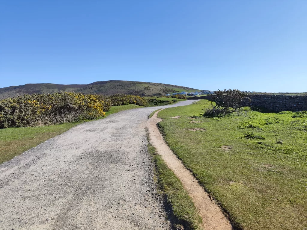 A scenic pathway leading through lush green fields with a clear blue sky in Wales, showcasing the natural beauty of the area near Worms Head.