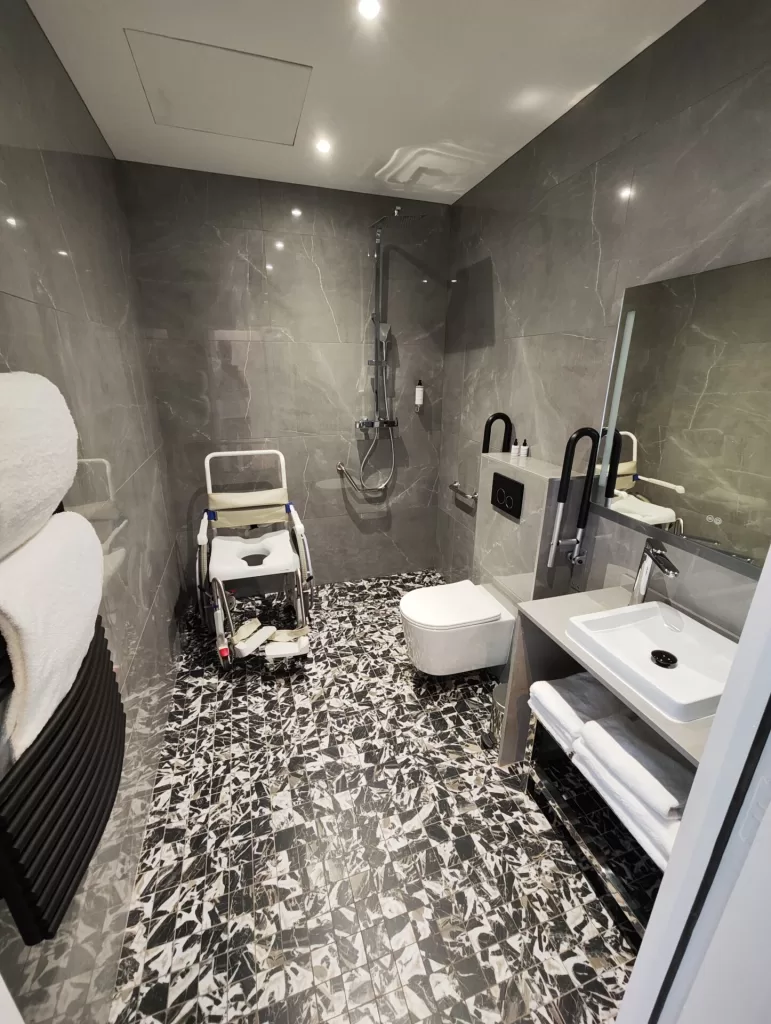 Accessible bathroom featuring a roll-in shower, grab bars, a shower chair, and a modern toilet in a stylish setting.