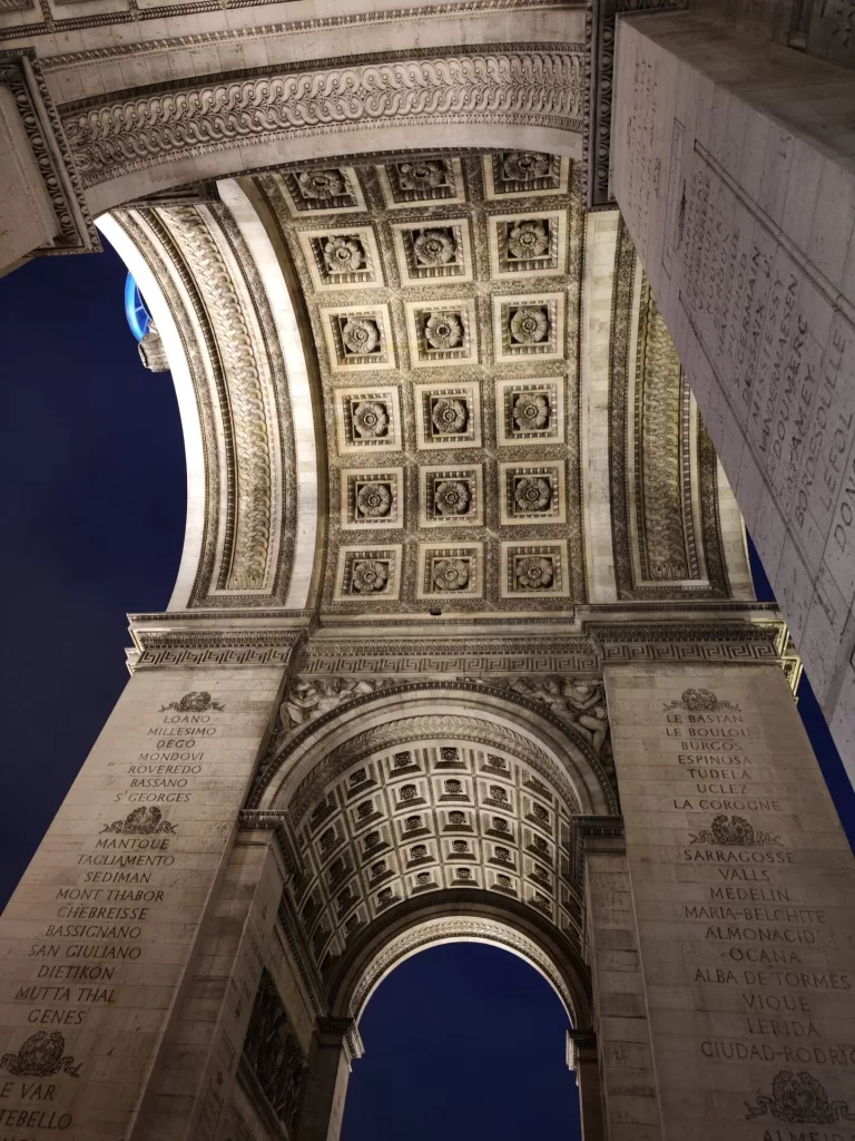 View of the intricate ceiling and columns of the Arc de Triomphe in Paris at night, with soft lighting illuminating the details.
