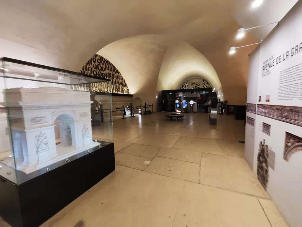 Interior view of an exhibition space displaying a model of the Arc de Triomphe, surrounded by informational panels and exhibits.