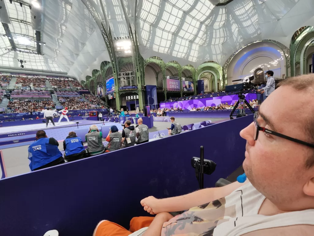 A spectator watching a Taekwondo match during the Olympic games at the Grand Palais, showcasing the vibrant atmosphere and competition in the background.
