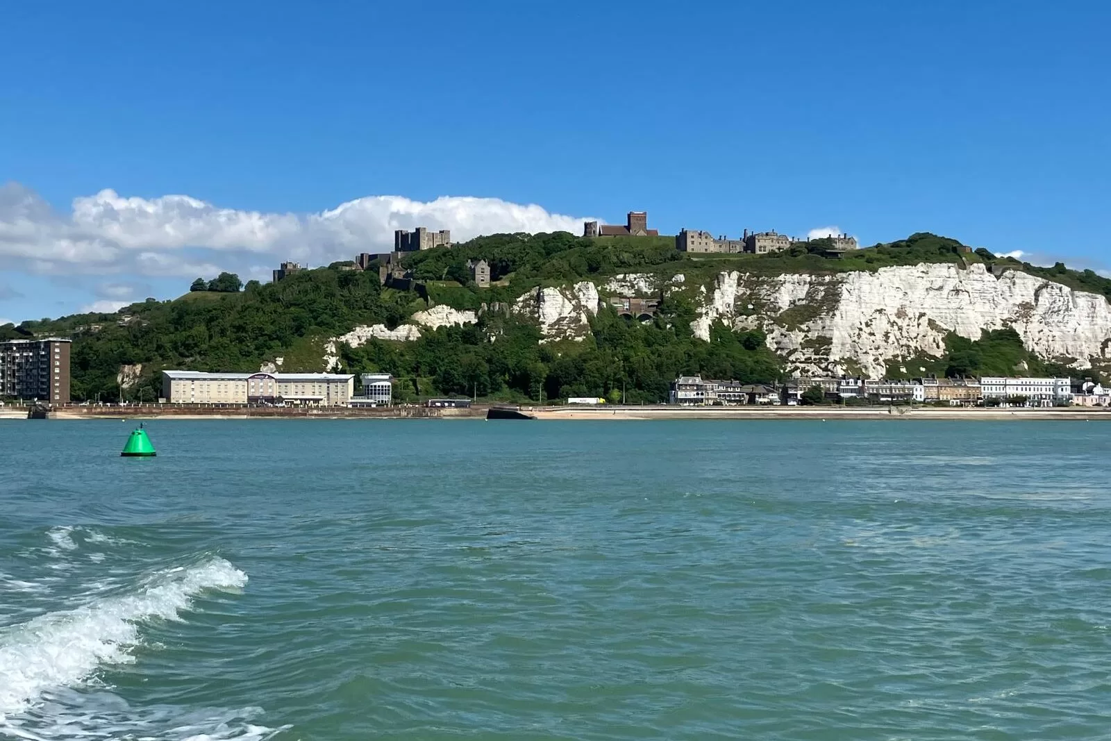 View of the White Cliffs of Dover and the surrounding buildings from the water on a sunny day.