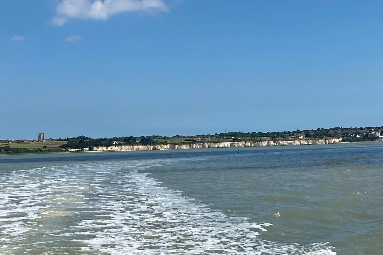 A view of the White Cliffs of Dover from a boat, with waves in the foreground and a clear blue sky.