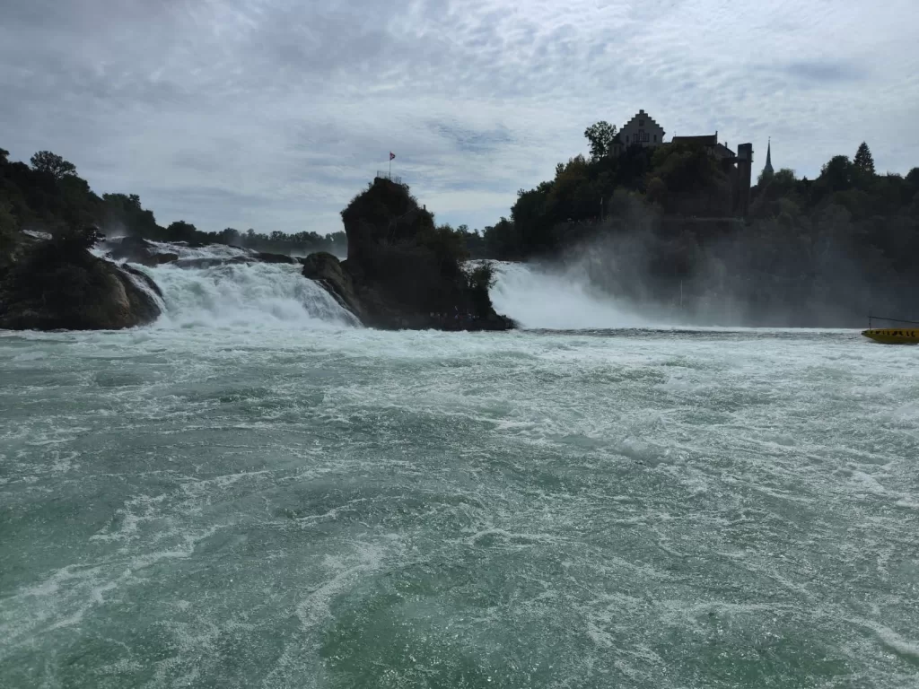View of the Rhine Falls, the largest waterfall in Europe, with powerful water cascading down and mist rising into the air.