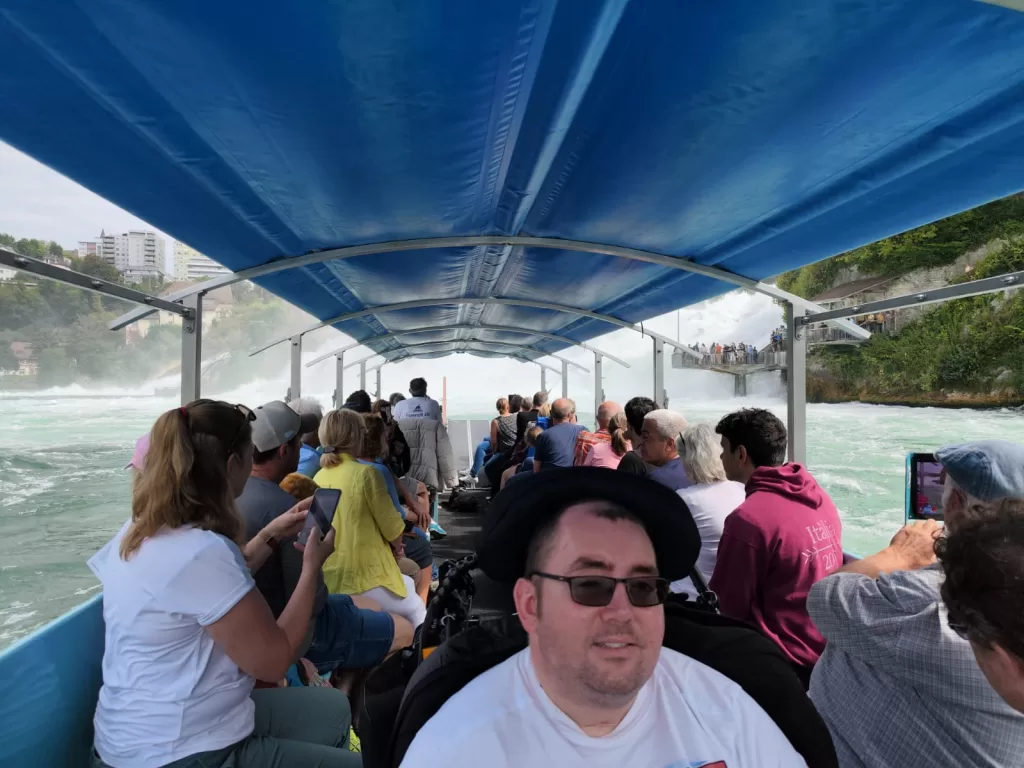 View from inside a boat approaching Rhine Falls, showing passengers and the waterfall mist in the distance.