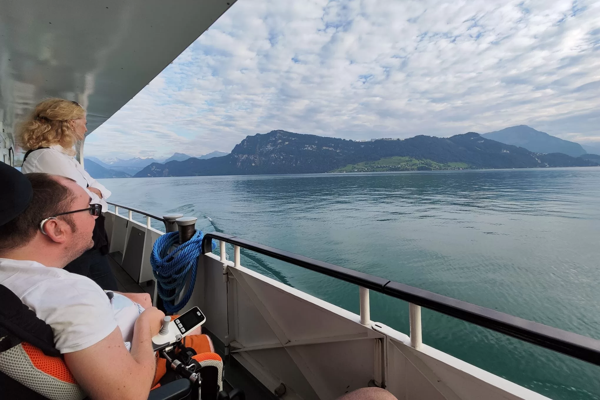 A person in a wheelchair looking out at a scenic view of mountains and water from a ferry.