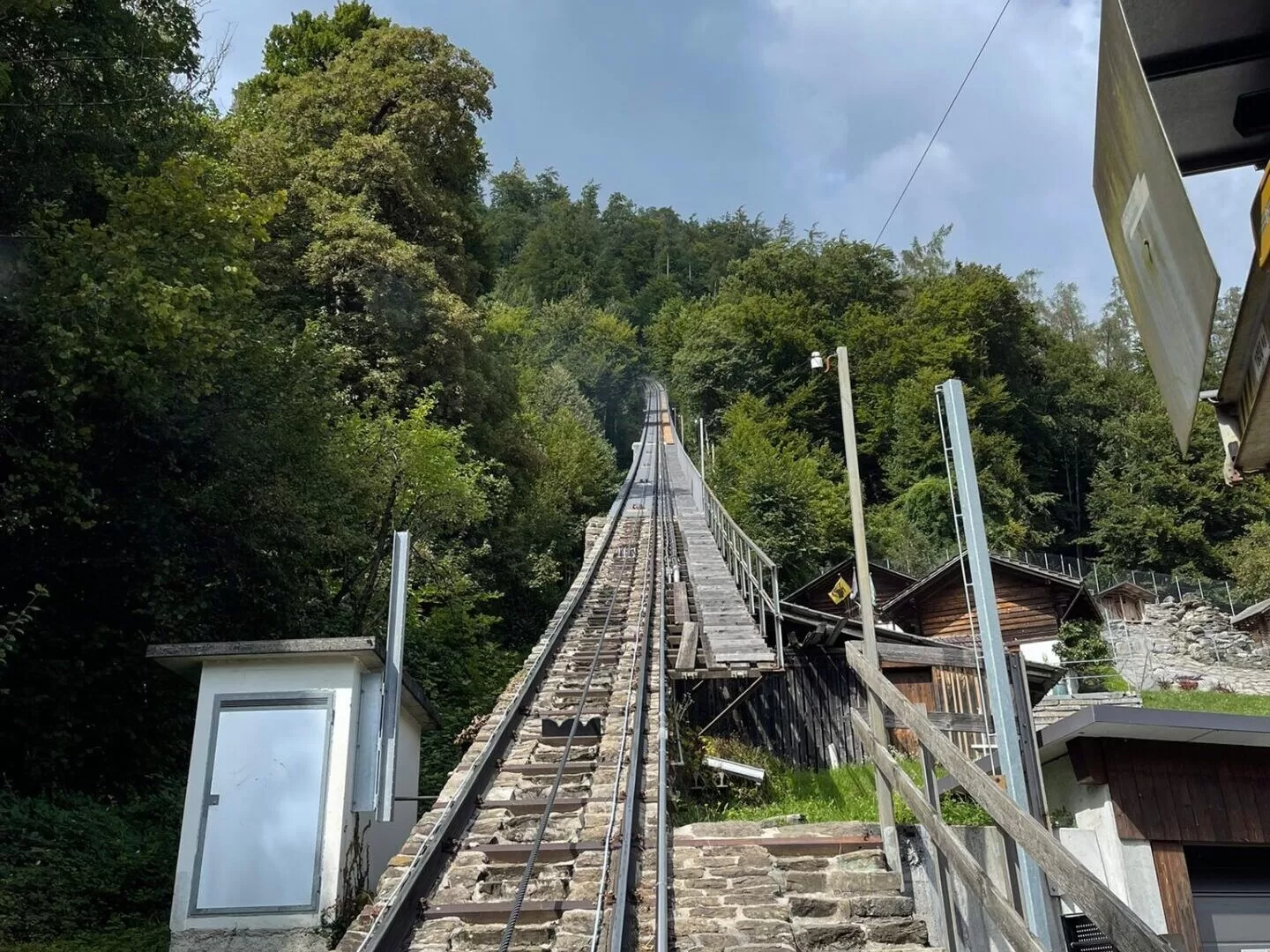 View of a funicular railway track ascending through a forested area, with wooden structures on either side.