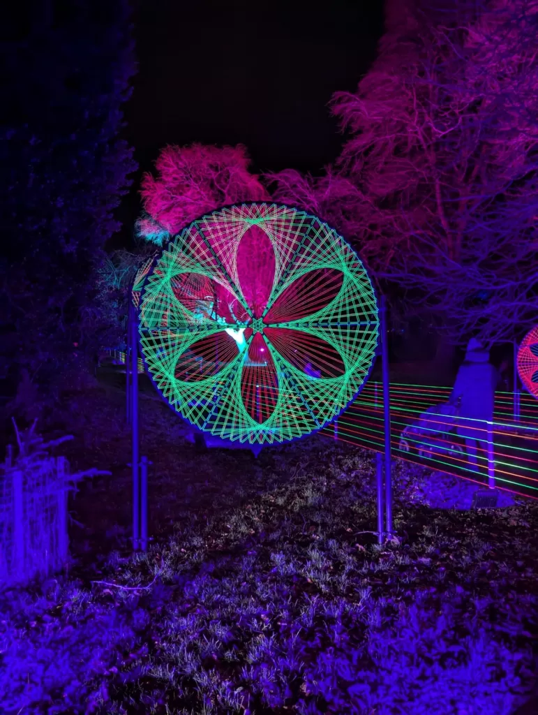 Colorful illuminated flower-shaped display with intricate patterns, set against a dark backdrop during a Christmas event.