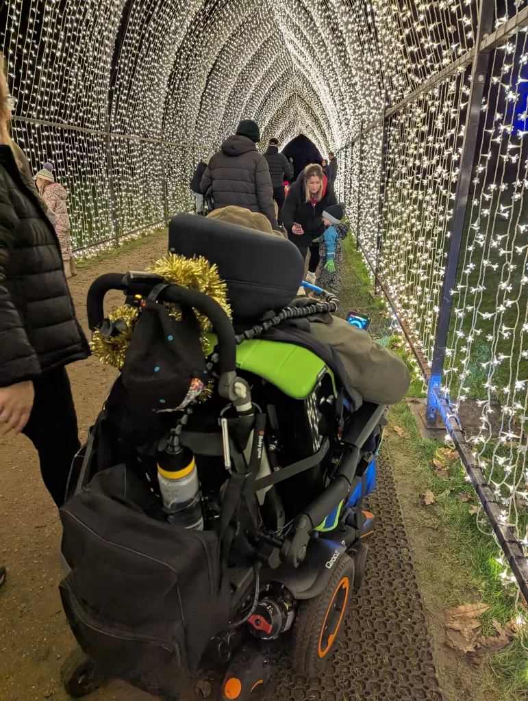 A festive light tunnel at Belton House, with people walking through the illuminated display, including a wheelchair with decorations.