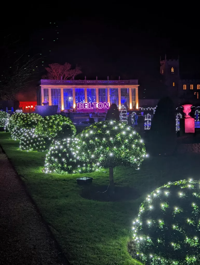 Illuminated garden with glowing trees and 'BELTON' sign in the background during Christmas light trail at Belton House.