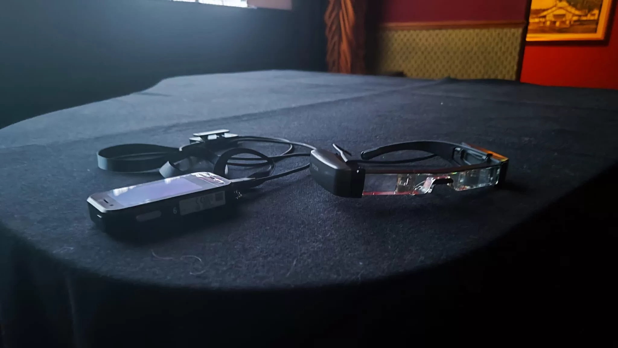 A pair of WatchWord subtitle glasses and a device on a table, designed to enhance cinema accessibility for hard-of-hearing individuals.