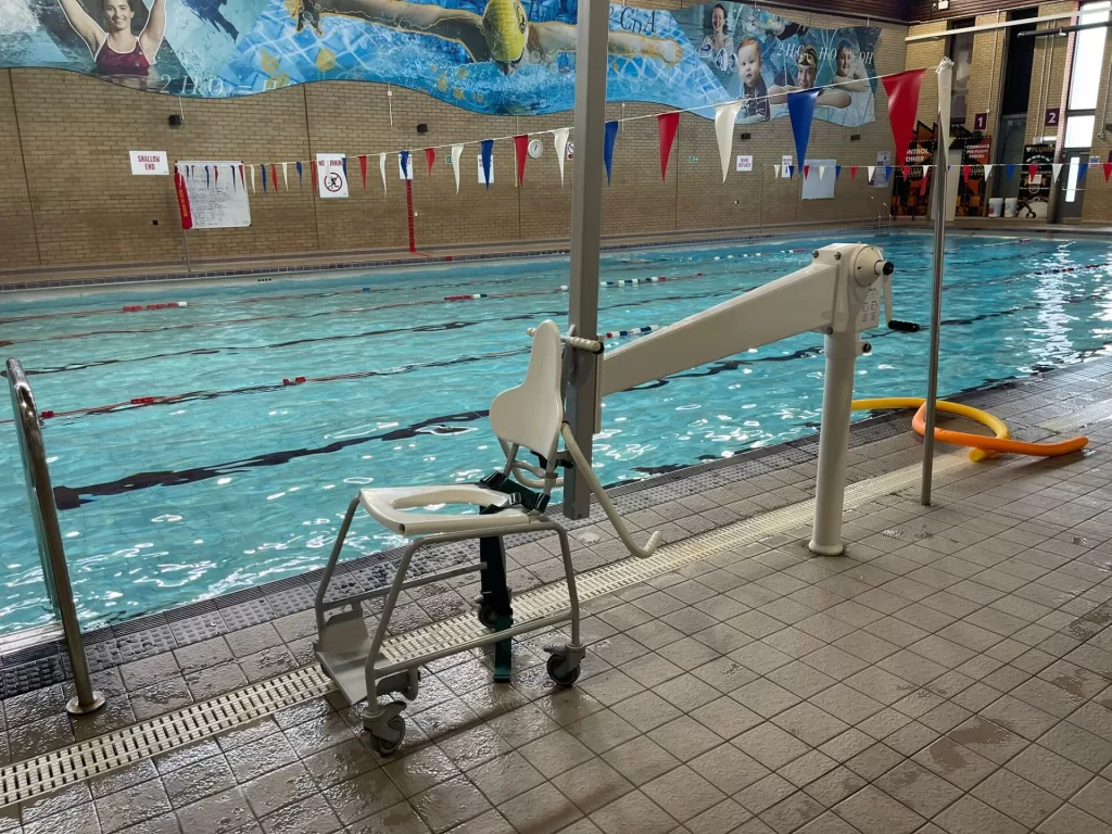 A poolside hoist with a shower chair positioned for accessibility by the swimming pool at One NK Leisure Centre.