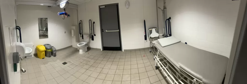 Interior of an accessible changing room equipped with a changing bed, Ceiling hoist, Shower, and shower chair