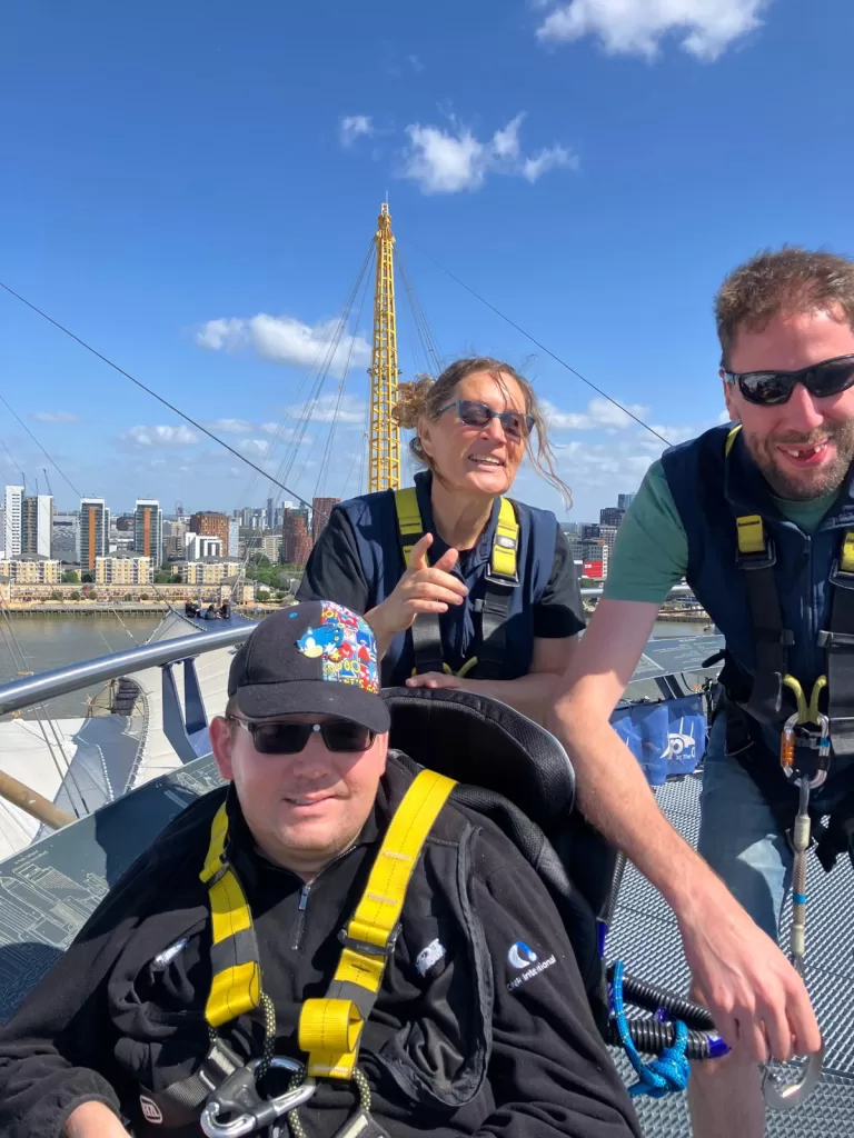 A group of three people experiencing the climb at the O2 Arena, with a clear blue sky and city skyline in the background.