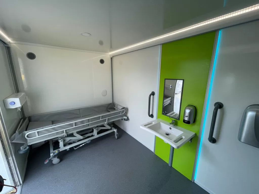 Interior of a Mobiloo, showing a changing table, sink, and mirror, designed for accessibility.