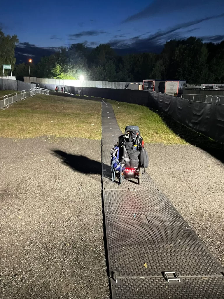 A person in a wheelchair navigating a smooth walkway at Heaton Park during a concert, with the night sky visible in the background.