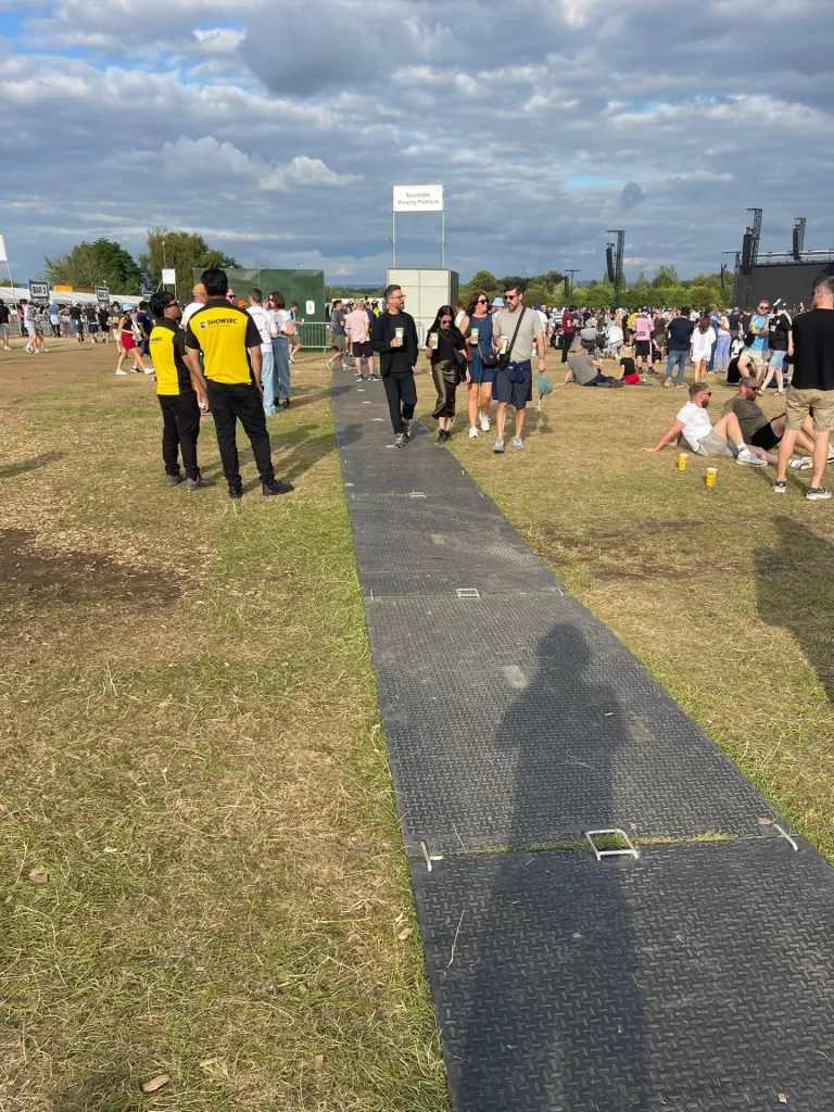 A smooth walkway leading to the accessible viewing platform at Heaton Park during an outdoor gig, with attendees walking in the background.