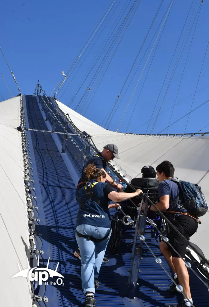 A group of people ascending the steep walkway at the O2 Arena during the 'Up at the O2' climb, with clear blue skies in the background.