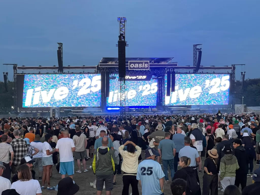 Crowd gathered at Heaton Park for the Oasis gig, with large screens displaying 'live '25' and a stage setup in the background.