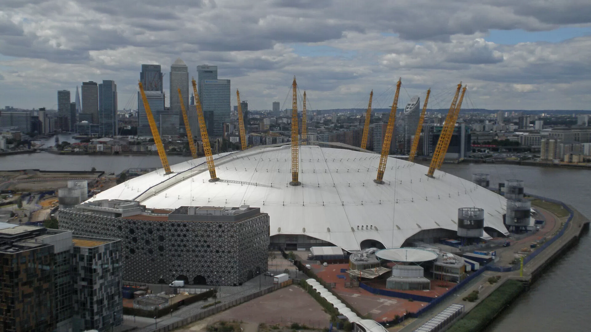 Aerial view of the O2 Arena in London, showcasing its distinctive dome shape and surrounding skyscrapers.